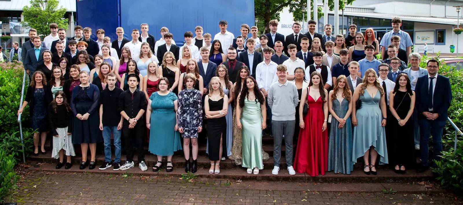 Gruppenfoto aller Abschlussklassen in festlicher Kleidung auf einer Außentreppe vor einem Gebäude