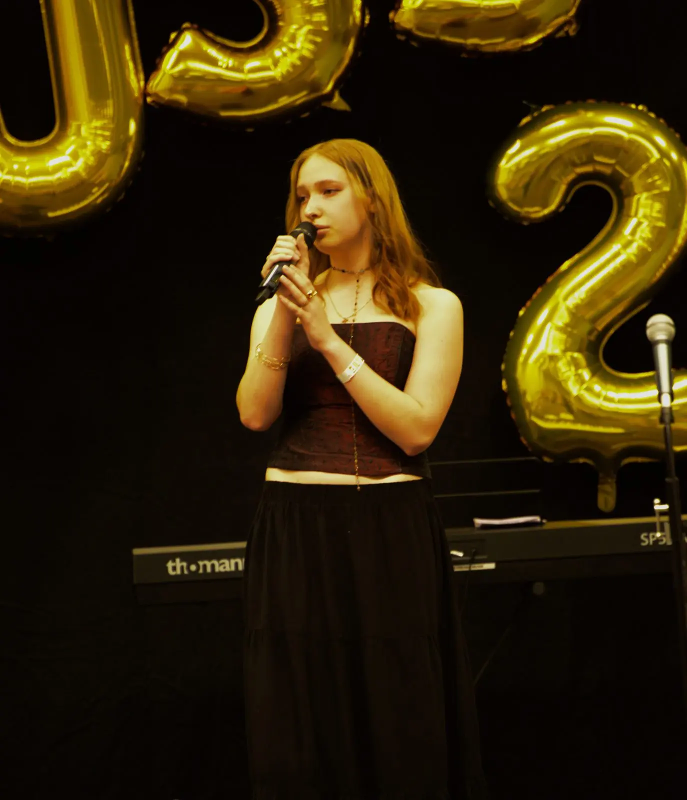 Eine Schülerin singt mit Mikrofon auf der Bühne vor goldenen Ballonbuchstaben