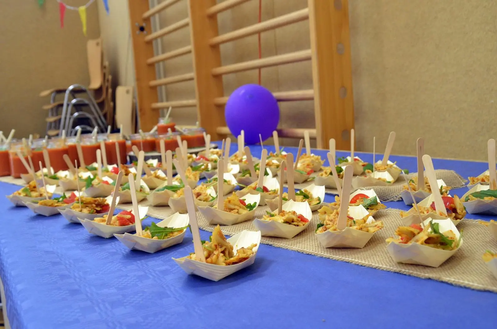 Buffet mit kleinen Snacks in Pappschalen auf blauem Tischtuch