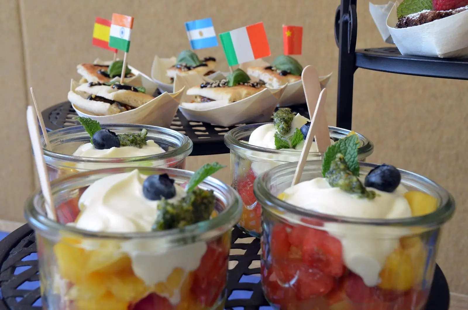 Gläser mit Obstdessert und Sahne, dahinter Snacks mit Länderflaggen