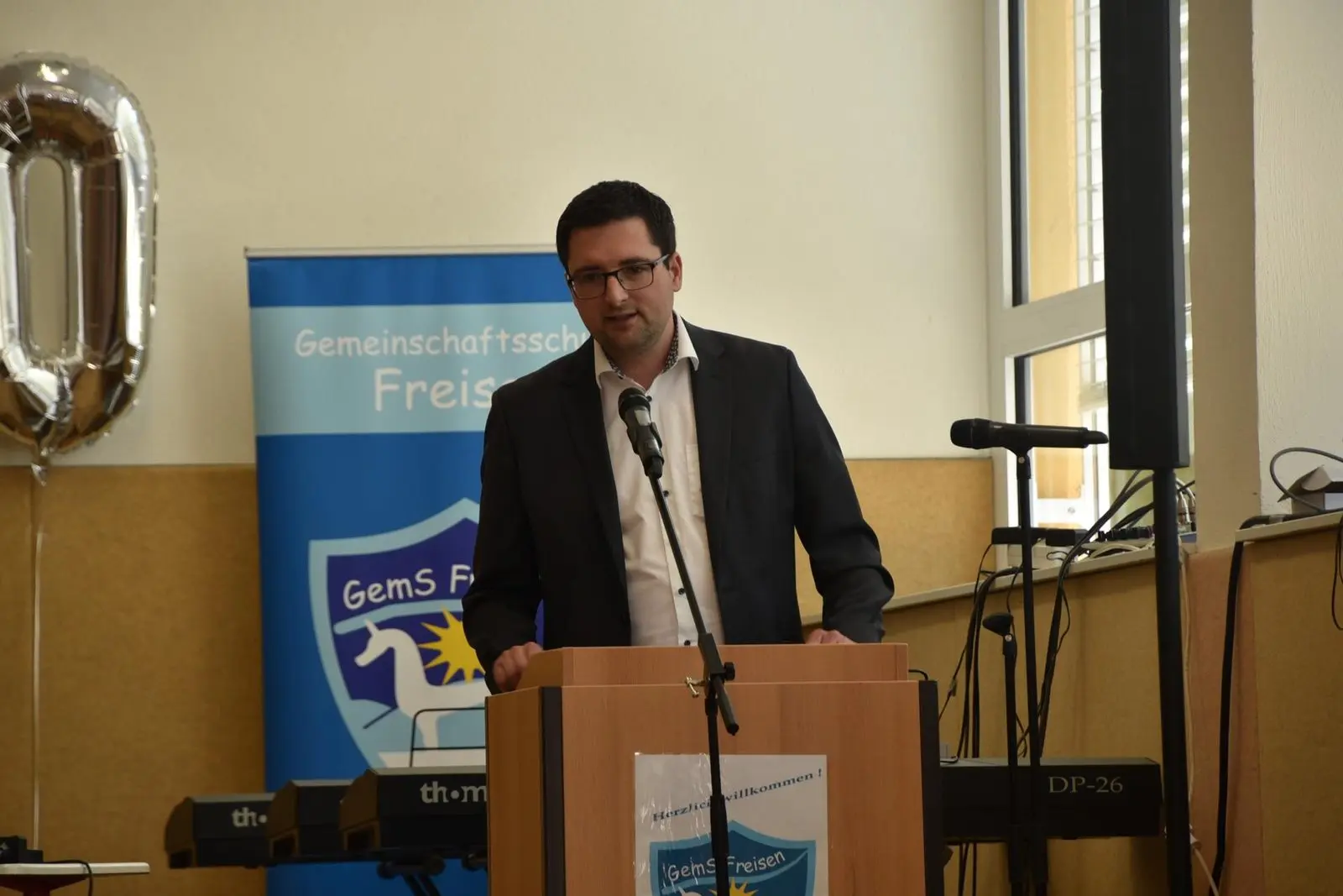 Mann spricht am Rednerpult vor einem Banner der Gemeinschaftsschule Freisen