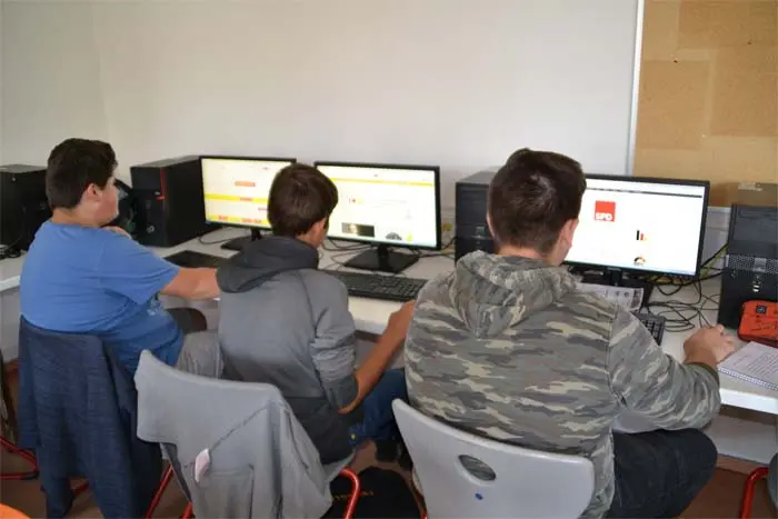 Drei Schüler sitzen an Computern, auf den Bildschirmen Webseiten, auf einem ein Parteilogo