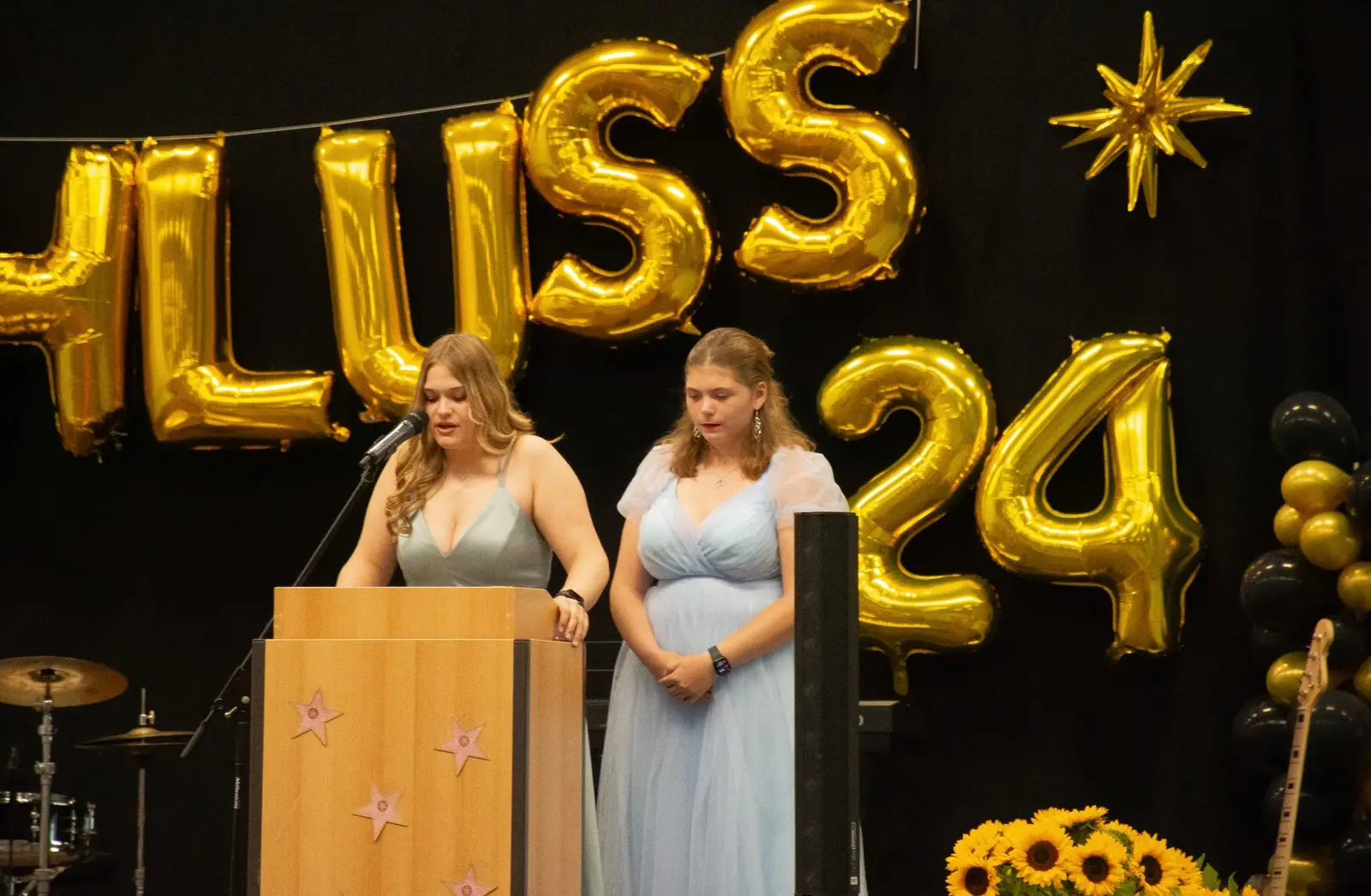 Schülerin im mintgrünen Kleid spricht am Rednerpult, daneben eine Mitschülerin im hellblauen Kleid