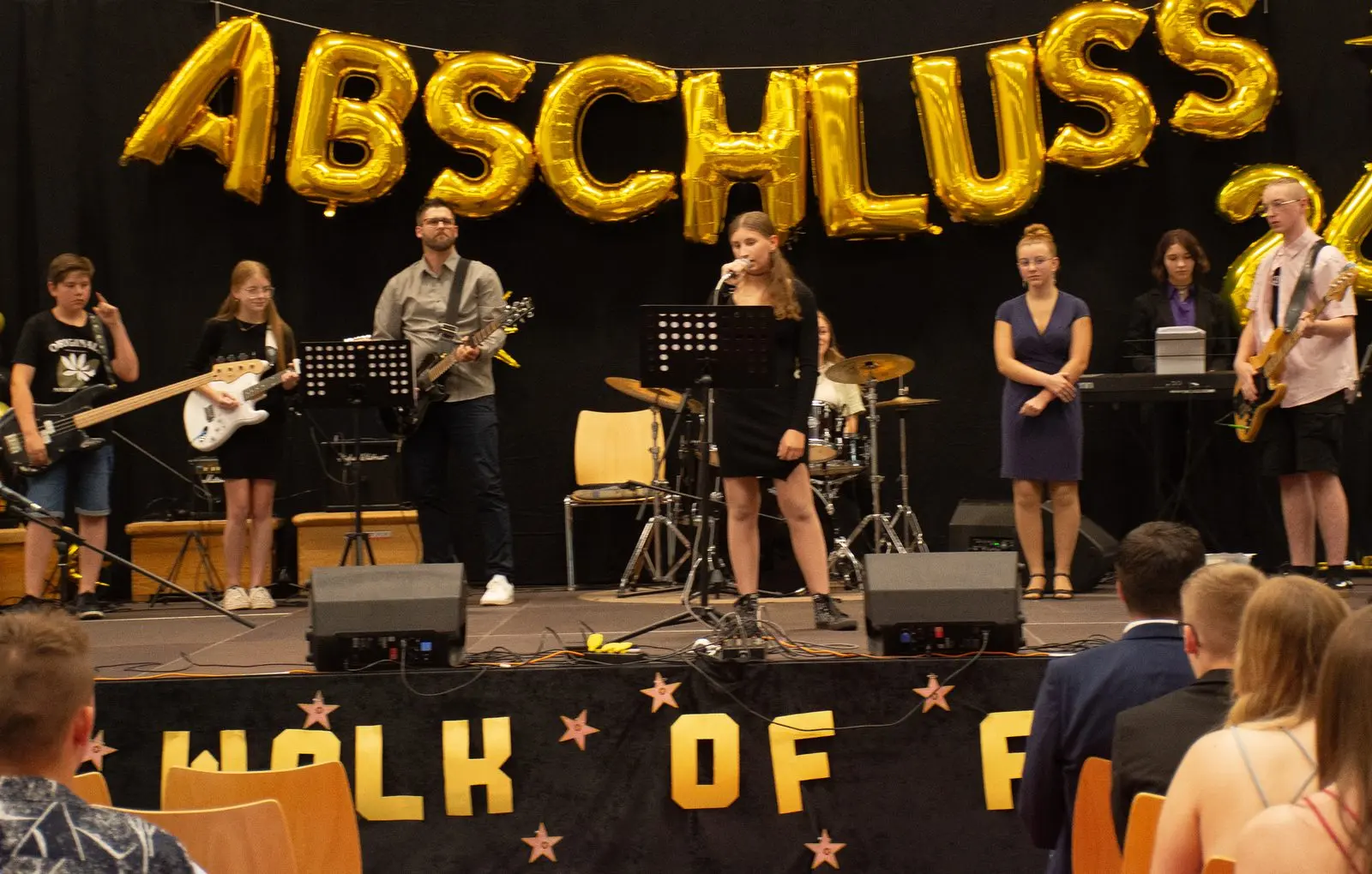 Schulband spielt, in der Mitte singt eine Schülerin im schwarzen Kleid, links Gitarren