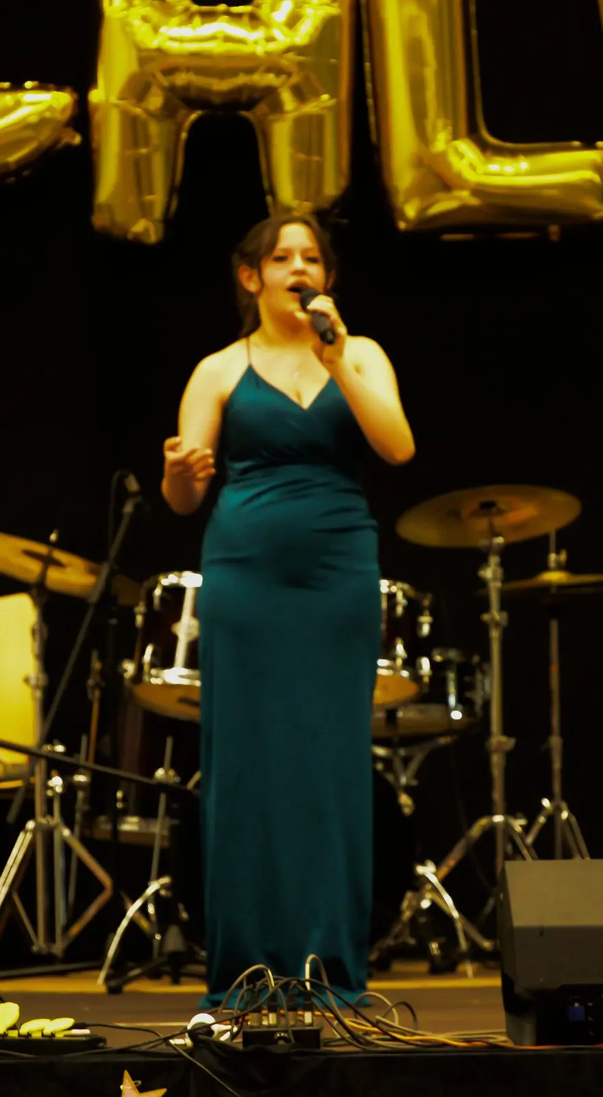 Eine Schülerin im langen dunkelgrünen Kleid singt mit Mikrofon auf der Bühne