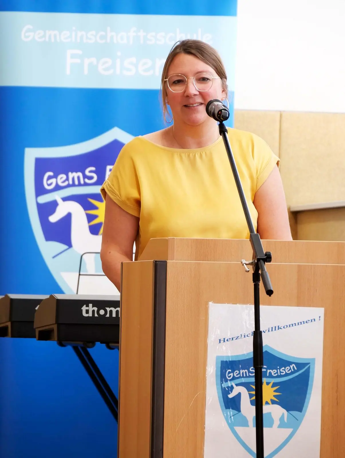 Frau spricht am Rednerpult vor dem Banner der Gemeinschaftsschule Freisen