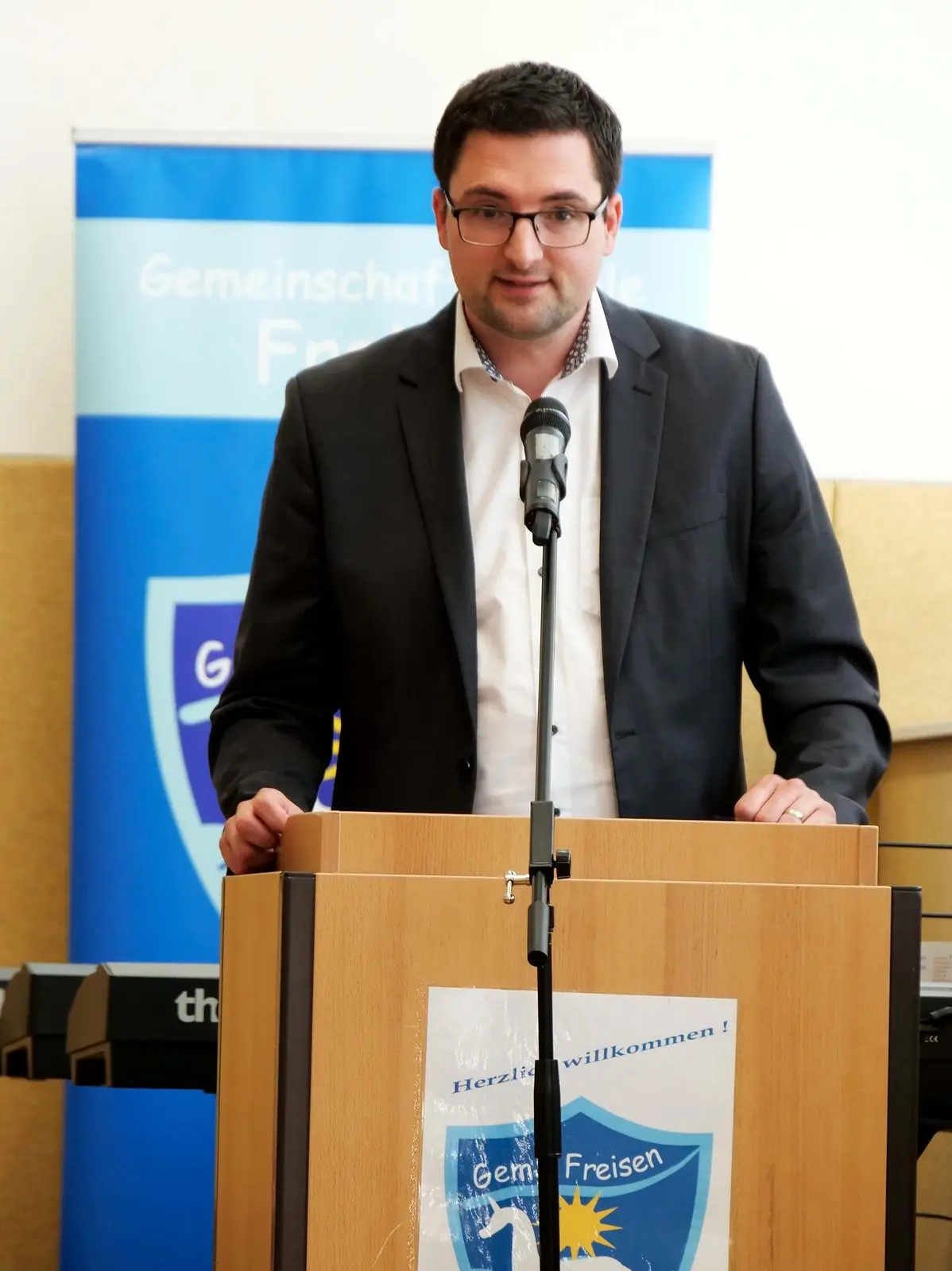 Mann spricht am Rednerpult vor dem Banner der Schule