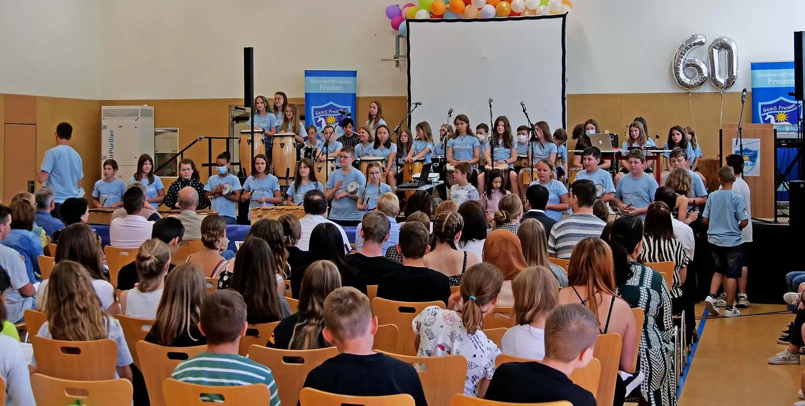 Publikum und Musikklasse in der Sporthalle, Ballons in Form der Zahl 60