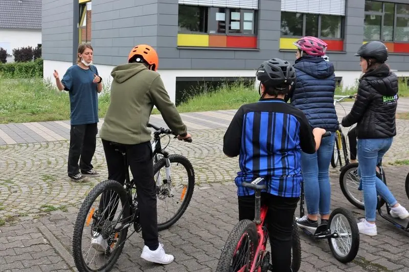 Eine Frau erklärt einer Gruppe mit Fahrrädern und Tretrollern etwas