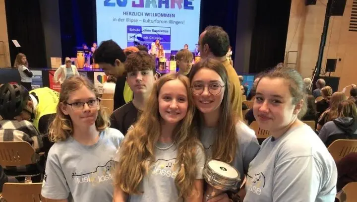 Fünf Jugendliche in MusiKlasse-T-Shirts vor der Bühne, auf der Leinwand „20 Jahre – Herzlich willkommen in der Illipse“
