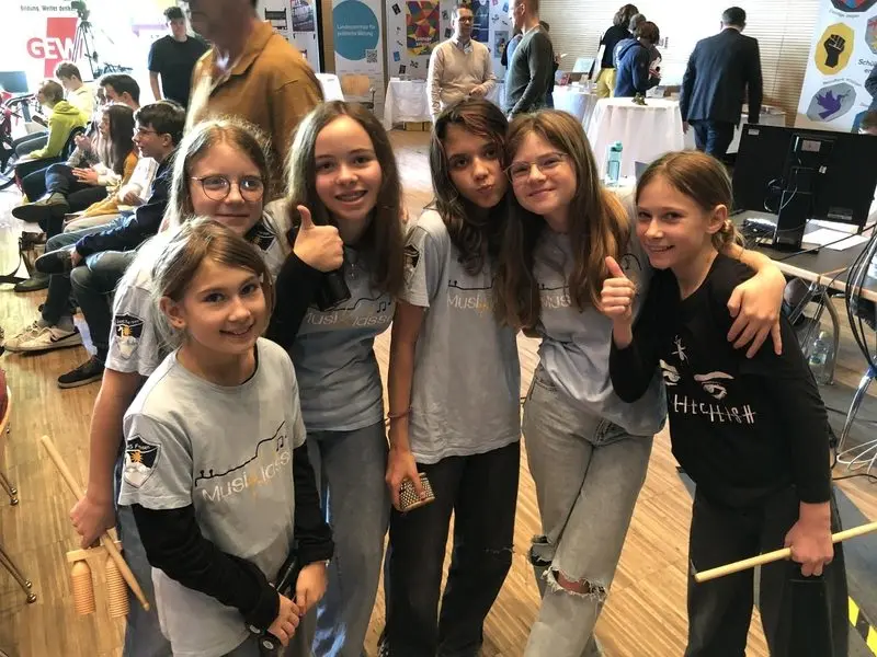 Schülerinnen in MusiKlasse-T-Shirts mit Percussion-Instrumenten, einige zeigen den Daumen nach oben