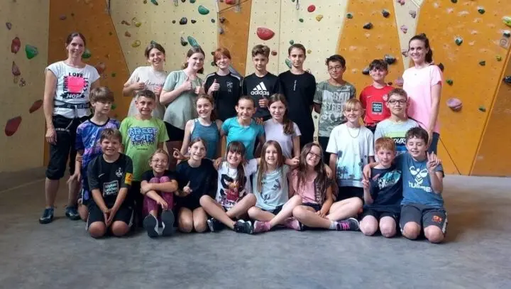 Gruppenfoto der Klasse mit zwei Erwachsenen vor einer Kletterwand in der Kletterhalle