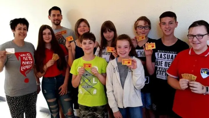 Schülerinnen und Schüler und Erwachsene halten Humanity Cards in die Kamera