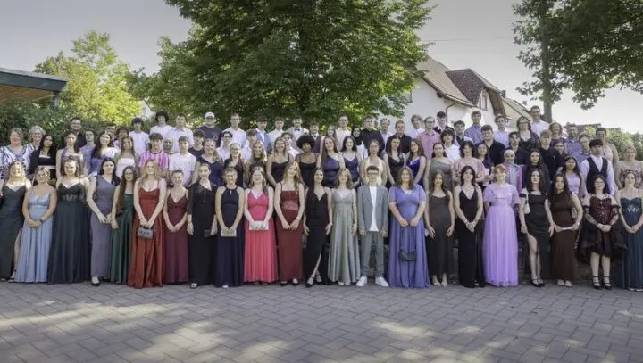 Großes Gruppenfoto der Abschlussschülerinnen und -schüler in festlicher Kleidung im Freien vor Bäumen