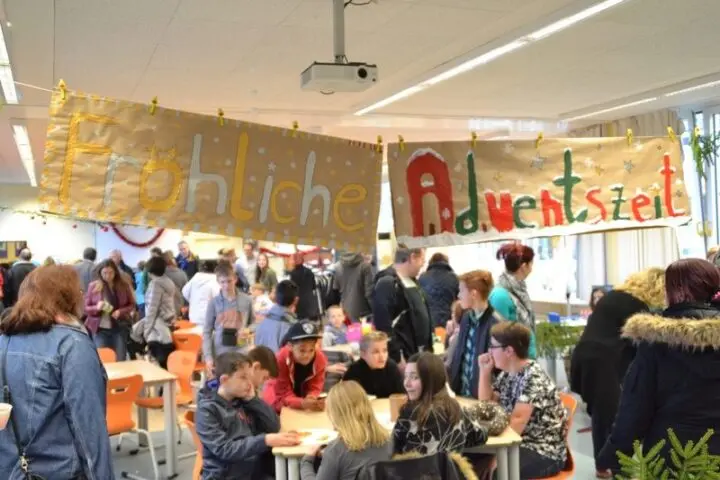 Adventsbasar: voller Raum unter Bannern „Fröhliche Adventszeit“, Besucher an Tischen