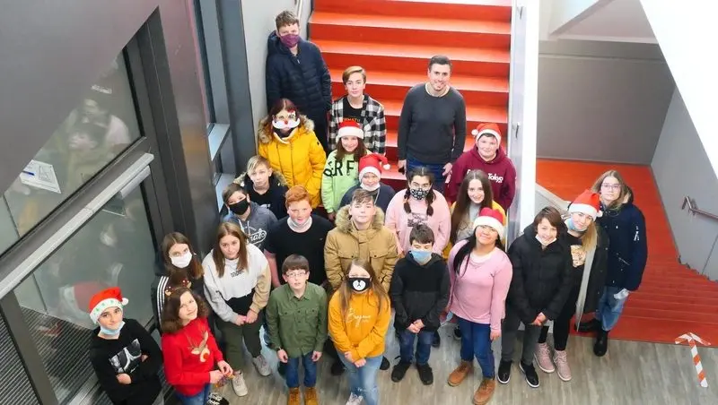 Klasse mit Lehrer im Treppenhaus von oben fotografiert, einige tragen Weihnachtsmützen und Masken