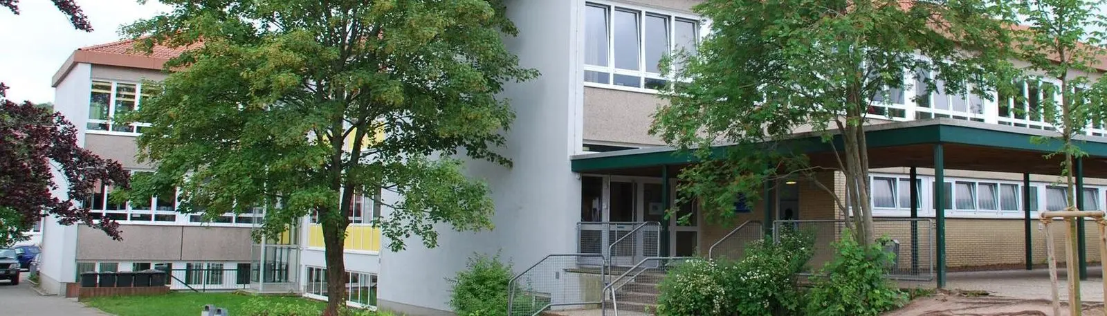 Außenansicht des Schulgebäudes mit Bäumen und überdachtem Eingangsbereich