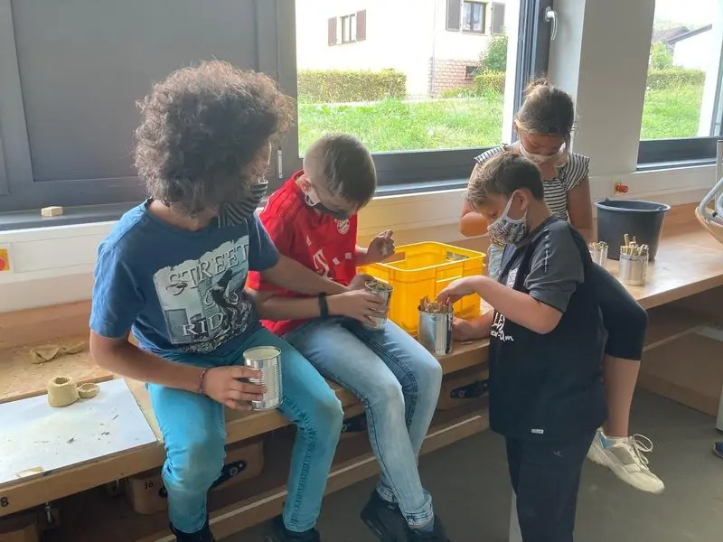 Kinder befüllen Blechdosen mit Pflanzenstängeln für Insektenhotels an einer Werkbank