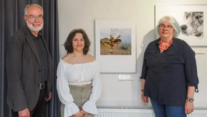 Junge Frau in der Ausstellung neben einem gerahmten Froschfoto, links und rechts zwei Erwachsene