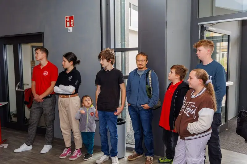 Jugendliche, ein Erwachsener und ein kleines Kind stehen nebeneinander im Foyer und hören zu