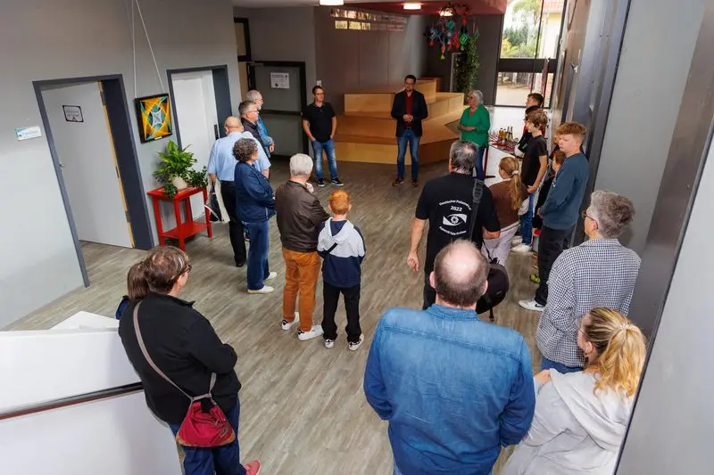 Besucherinnen und Besucher stehen im Halbkreis im Schulfoyer und hören einem Redner zu
