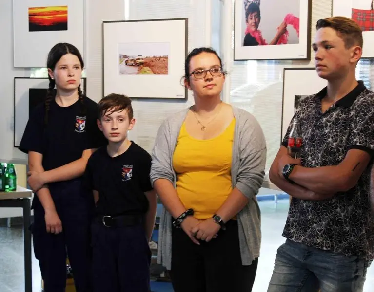 Vier Personen stehen vor gerahmten Fotos der Ausstellung und hören zu