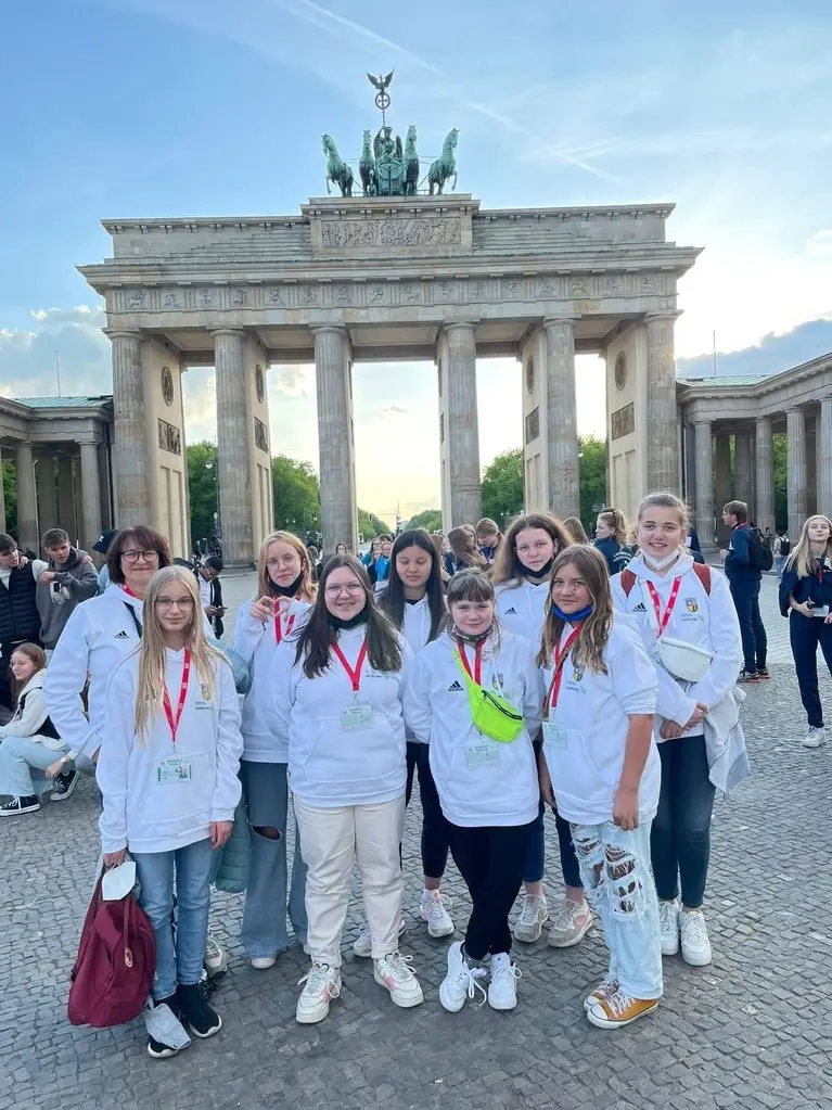 Mädchenmannschaft in weißen Jacken mit Betreuerin vor dem Brandenburger Tor