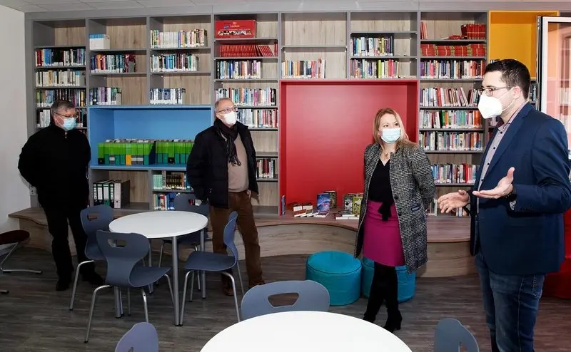Vier Erwachsene mit Masken in der neuen Schülerbibliothek vor bunten Bücherregalen