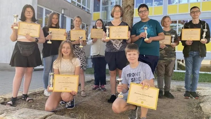 Schülerinnen und Schüler mit Pokalen und Urkunden „First Class National Honours“ vor dem Schulgebäude