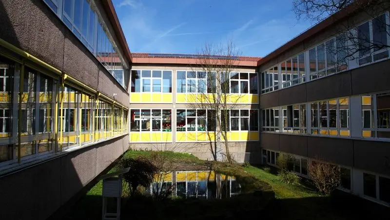 Innenhof des Schulgebäudes mit gelben Fensterbändern und kleinem Teich