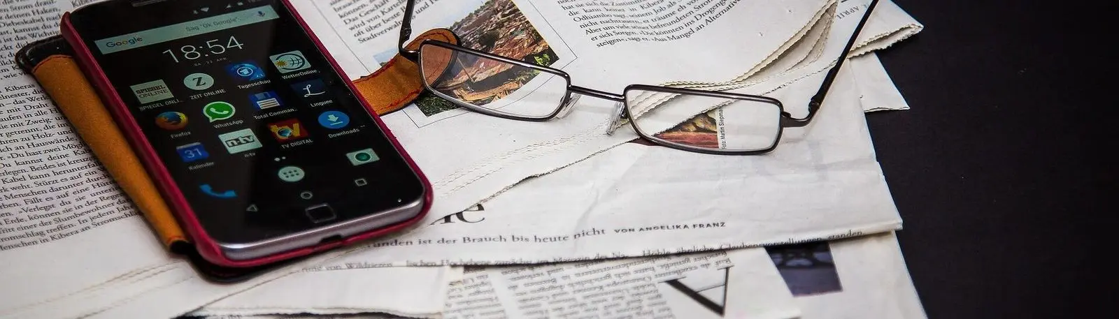 Smartphone und Brille liegen auf aufgeschlagenen Zeitungen
