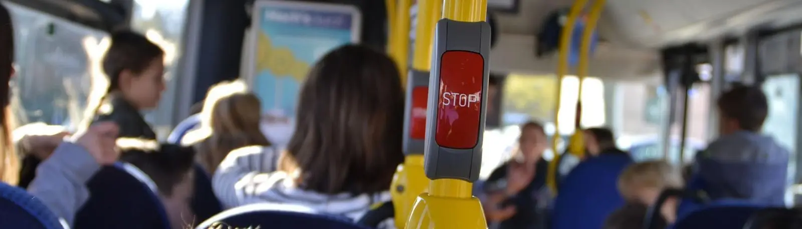 Fahrgäste in einem Bus, im Vordergrund eine Haltestange mit roter Stopptaste