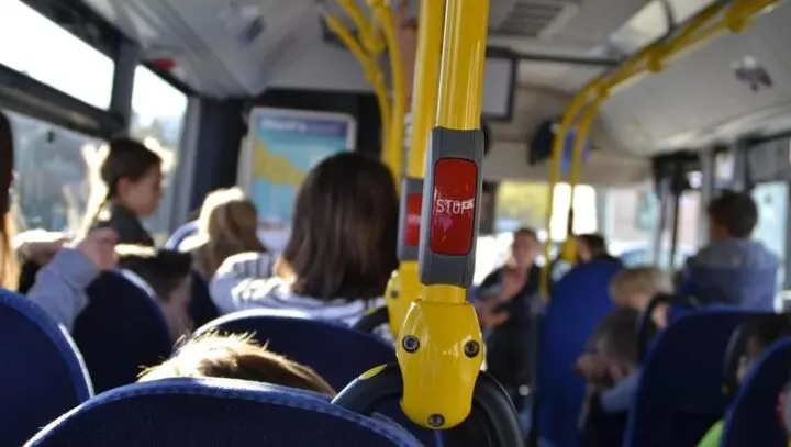 Blick durch einen Linienbus mit Fahrgästen und gelben Haltestangen mit Stopp-Taster
