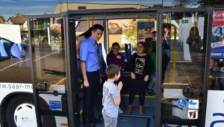 Kinder stehen in der offenen Tür eines Saar-Mobil-Busses, davor ein Busfahrer und ein Junge