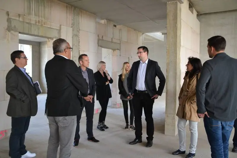 Besuchergruppe steht im Gespräch im Rohbau eines Gebäudes
