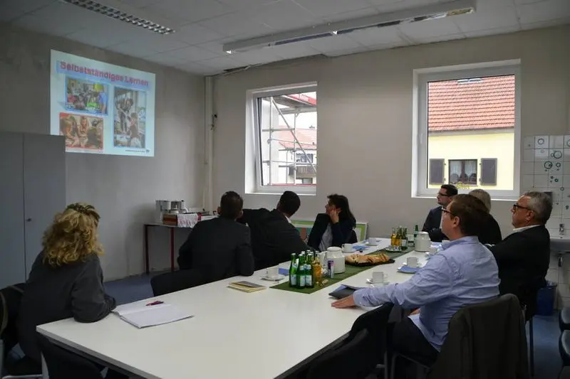 Besuchergruppe am Konferenztisch verfolgt eine Präsentation zum Thema „Selbstständiges Lernen“