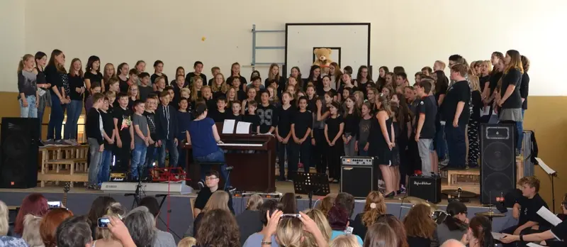 Großer Chor auf der Bühne der Turnhalle mit Klavier und Verstärkern, im Vordergrund das Publikum