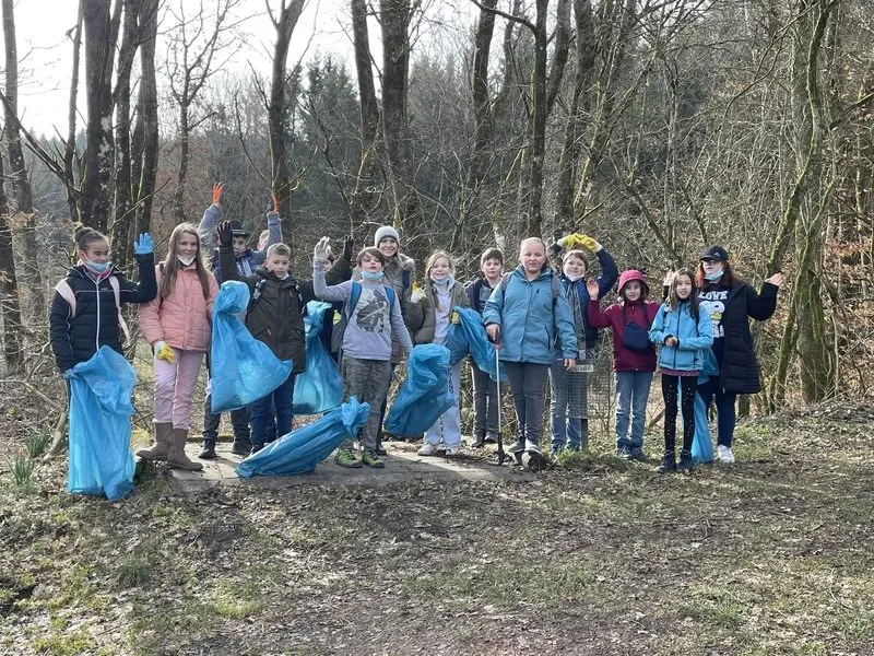 Gruppe von Kindern mit blauen Müllsäcken und Handschuhen winkt im Wald