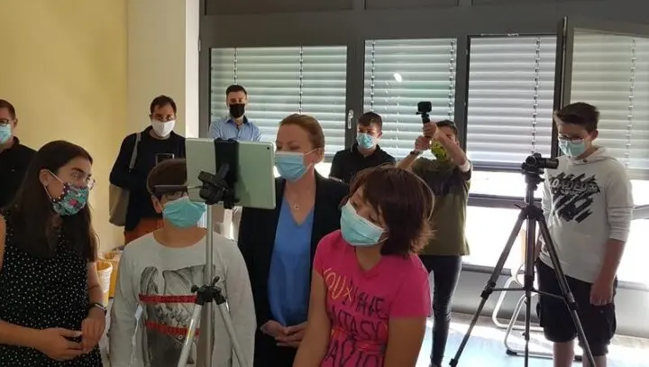 Besucherin mit Maske beobachtet Jugendliche an Tablet und Kameras auf Stativen