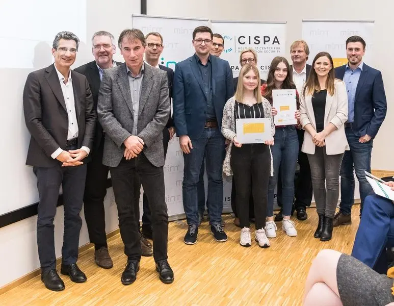 Gruppe von Erwachsenen und Jugendlichen vor CISPA- und MINT-Aufstellern, zwei Jugendliche halten Urkunden