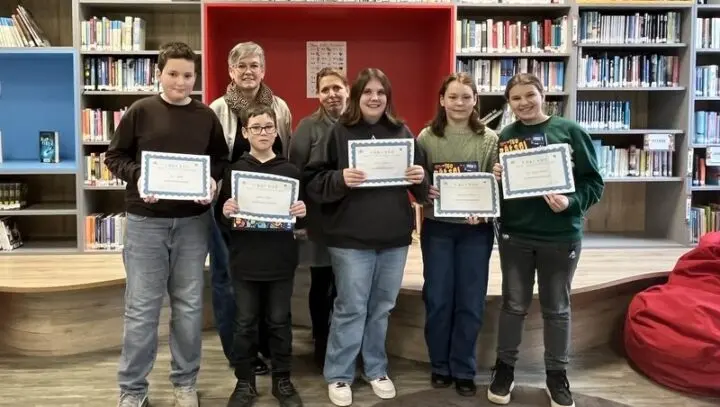 Sechs Schülerinnen und Schüler halten Urkunden in der Schulbibliothek, dahinter zwei Frauen