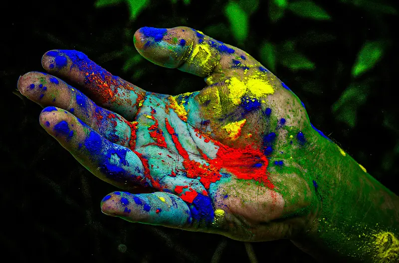 Fotografie: mit bunter Farbe bemalte Hand vor grünem Hintergrund