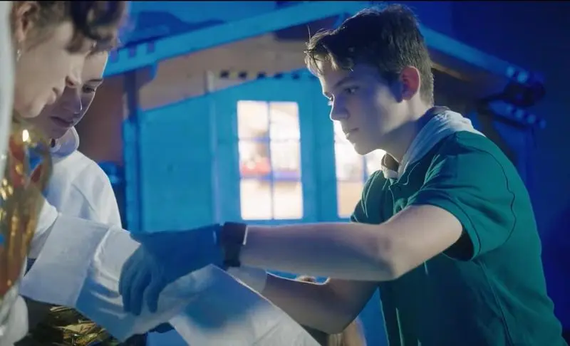 Jugendlicher mit Einmalhandschuhen legt einer Person einen Verband an, Standbild aus dem Imagefilm