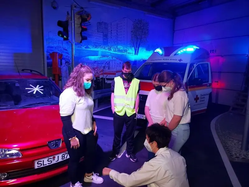 Jugendliche in Sanitätskleidung und Warnweste zwischen rotem Auto und Rettungswagen in blauem Licht