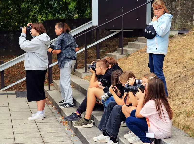 Jugendliche fotografieren auf einer Treppe sitzend und stehend, daneben eine Betreuerin