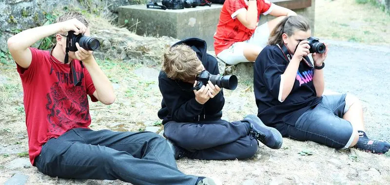 Drei Jugendliche fotografieren am Boden sitzend mit Spiegelreflexkameras, Nahaufnahme
