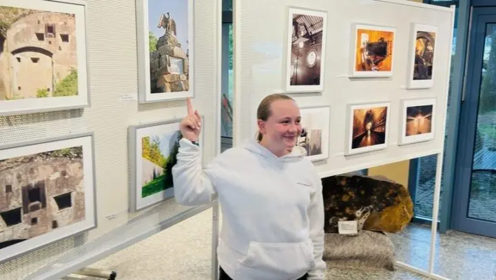 Schülerin zeigt lächelnd auf ein ausgestelltes Foto an einer Stellwand