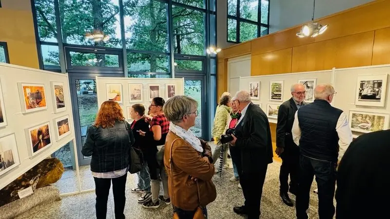 Besucherinnen und Besucher betrachten gerahmte Fotos an Stellwänden im Foyer