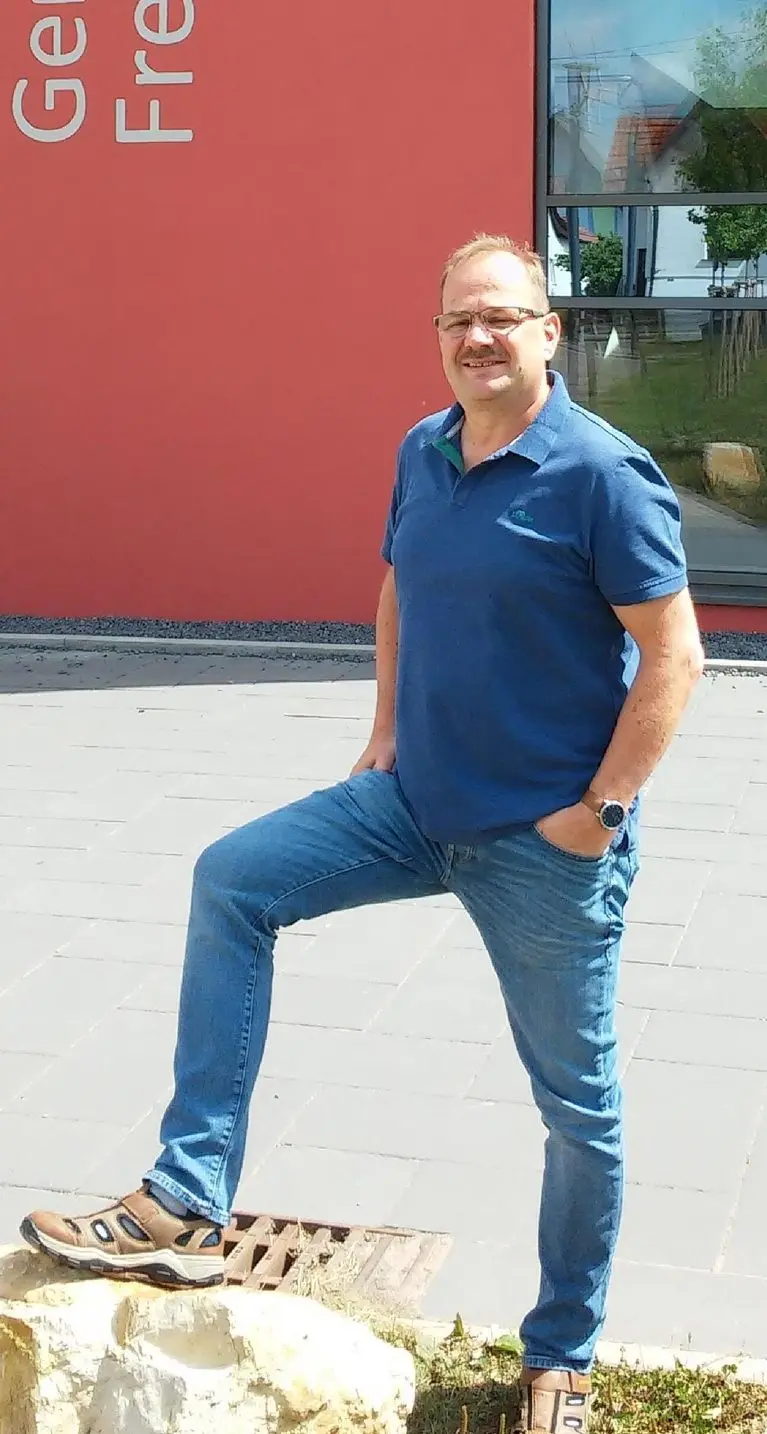 Ein Mann im blauen Poloshirt steht vor der roten Fassade des Schulgebäudes