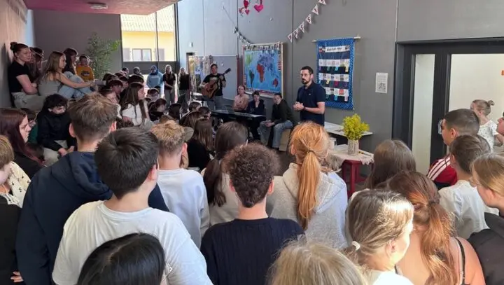 Viele Schülerinnen und Schüler versammelt im Foyer, vorne ein Sprecher, Gitarre und Keyboard